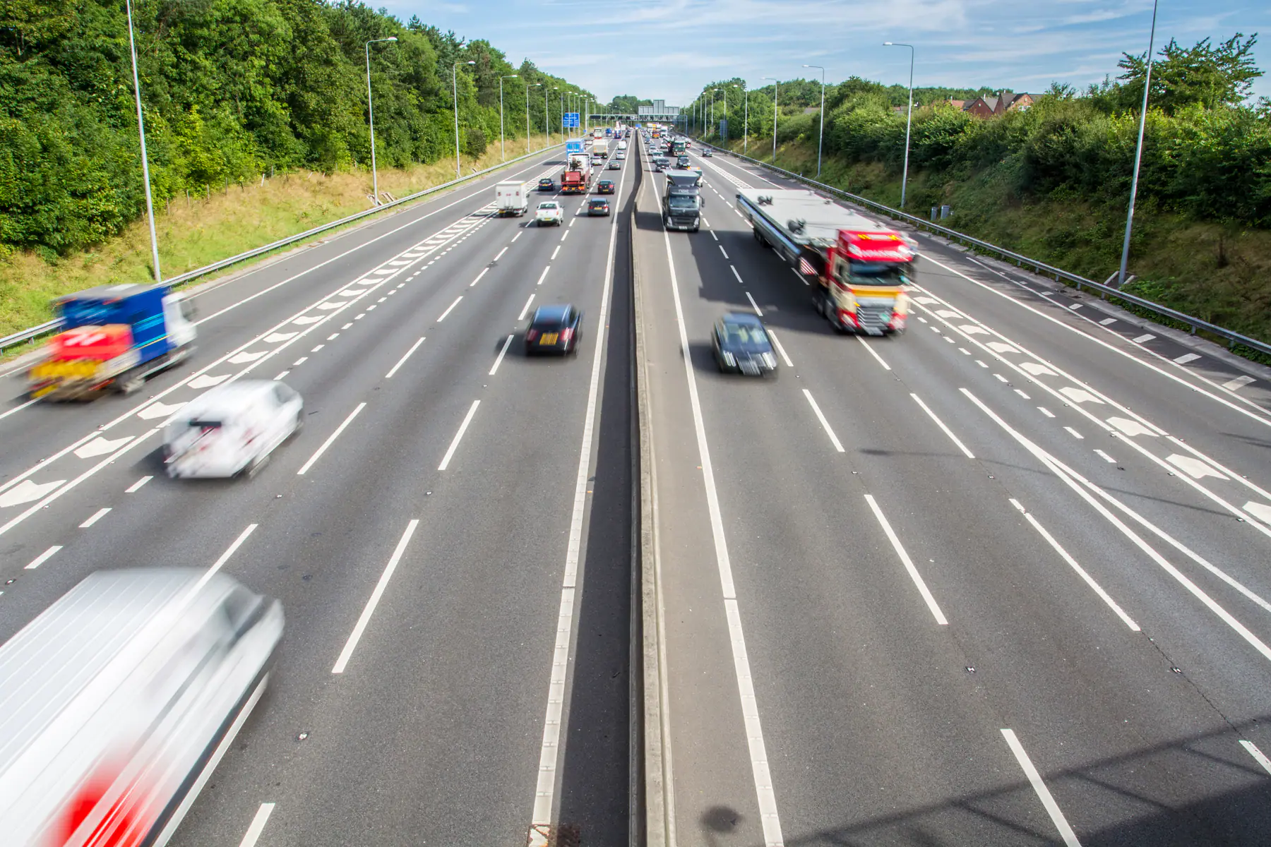 Cars and lorries travelling on a busy three-lane UK motorway lined with trees