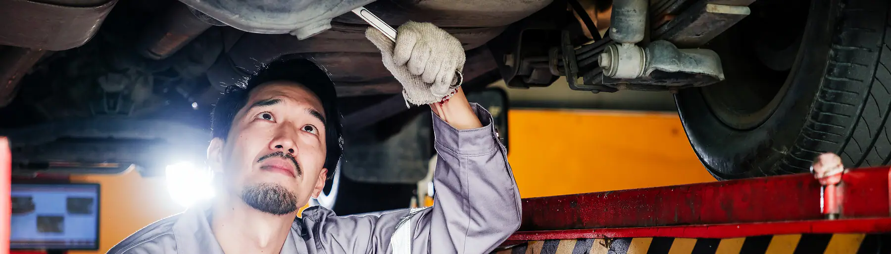 A mechanic with a spanner checking the underside of a car raised on a workshop lift