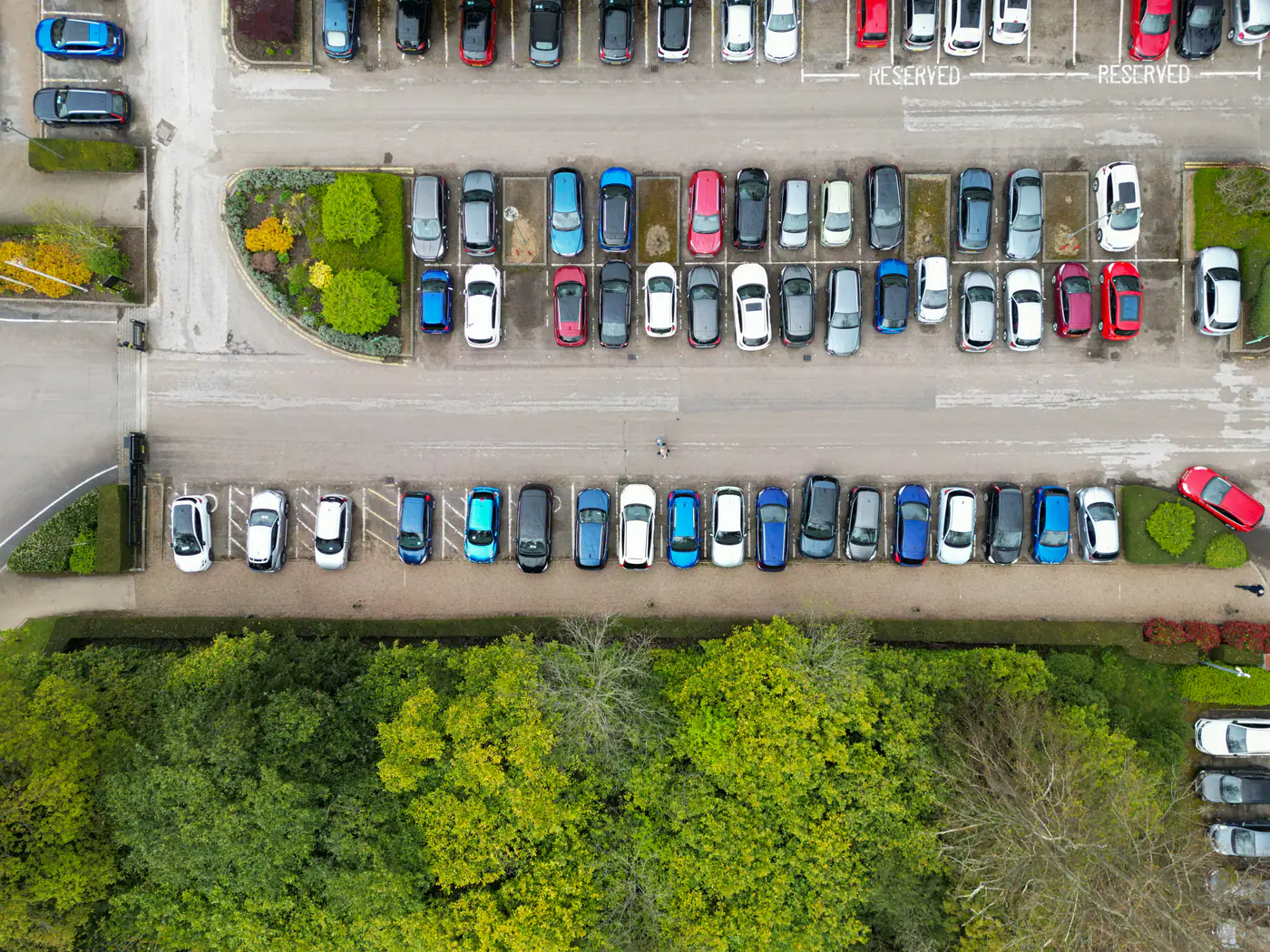 Top-down view of rows of parked cars in a car park beside trees in the English countryside